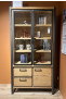 Die Vitrine „Metalo“ mit Glastüren und LEDs präsentiert Bücher und Dekoartikel vor einer orangefarbenen Wand.