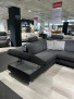 Ecksofa Planoform Nizza mit Stoff Vincent, offenem Stauraum und Querschläferfunktion in einem modernen Ausstellungsraum.