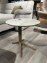 Beistelltisch Hagen mit Keramik-Glasplatte und Metallgestell in Bronze neben einem grauen Sofa auf einem Holzboden.