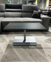 Couchtisch 1426-MMN-EST auf hellem Holzboden, vor einem grauen Sofa mit schwarzem Kissen.