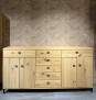 Das Sideboard Vilano Solero aus Ast-Eichenfurnier, 4 Schubladen/Türen, vor einer beige gemusterten Wand und einem grauen Boden.
