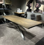 Esstisch „Mondo Natur Peristo“ mit Baumkante Natur und Edelstahlgestell, im Showroom zusammen mit Stühlen und Kunstwerken abgebildet.