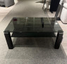 Der Couchtisch CUBICO mit Rauchglasplatte und schwarzen Beinen steht im Ausstellungsraum auf einem grauen Teppich.