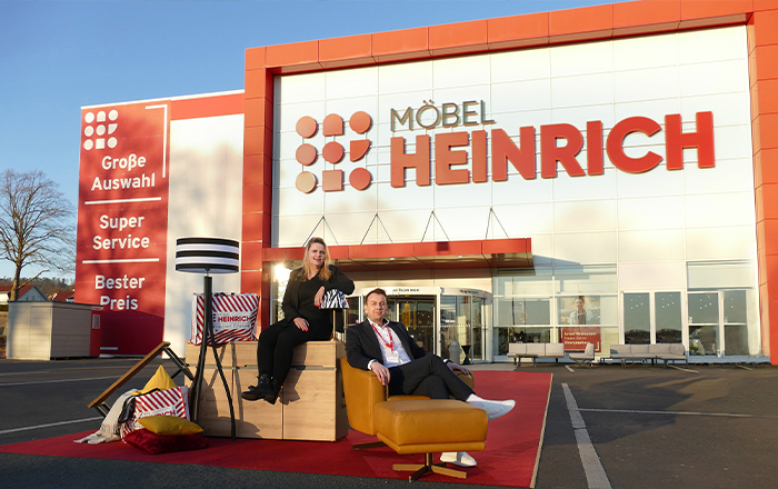 Außenansicht Möbel Heinrich Halen. Zwei Personen sitzen auf Möbeln vor dem Eingang.