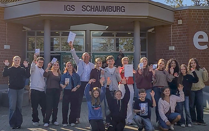 Eine Schülergruppe, eine Frau und ein Mann vor dem Schulgebäude der IGS Schaumburg.
