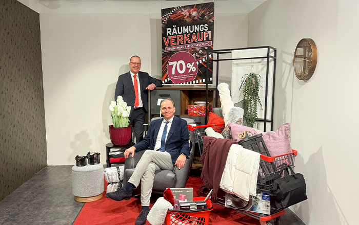 Zwei Männer mit Möbeln vor einem Räumungsverkaufsschild bei Möbel Heinrich