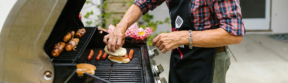 Jemand packt Brötchen und Bratwurst auf einen Grill