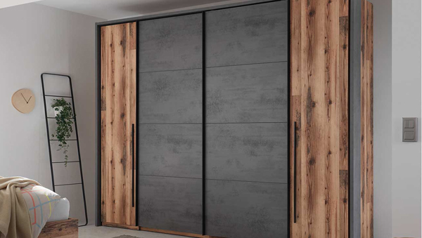 Stil Industrial Kleiderschrank Sarnthein mit Betonoptik, rustikalen Holzseiten und schwarzem Rahmen in einem Schlafzimmer