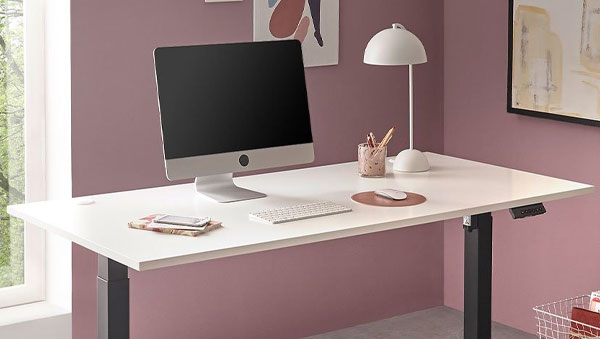 Weißer Schreibtisch mit schwarzen Beinen, Computer, Tastatur, Lampe, Stifthalter, Notizblock und Maus in Raum mit rosa Wänden