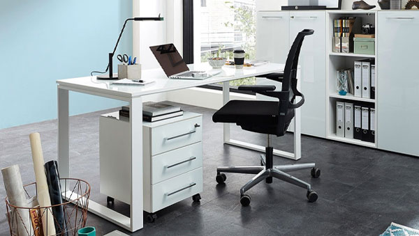 Moderner weißer Schreibtisch mit schwarzem Bürostuhl, Laptop, Schreibtischlampe und Rollcontainer in hellem Büro