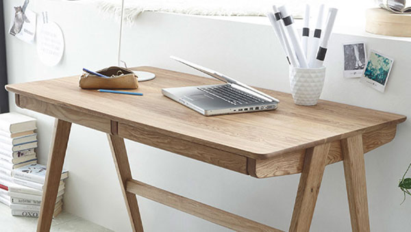 Massivholz-Schreibtisch mit schrägen Beinen, darauf ein Laptop, gerolltes Papier im weißen Behälter und ein Etui mit Stiften