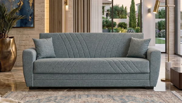 Graues Dreisitzer-Sofa Aiden mit dekorativer Steppung und zwei Kissen in einem modern eingerichteten Wohnzimmer mit großen Fenstern
