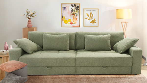 Grünes Big Sofa mit mehreren Kissen in einem hellen Wohnzimmer;