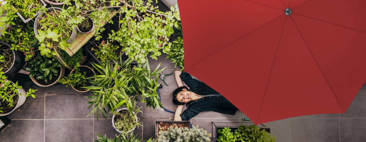 Eine Person liegt entspannt unter einem roten Sonnenschirm in einem grünen Garten