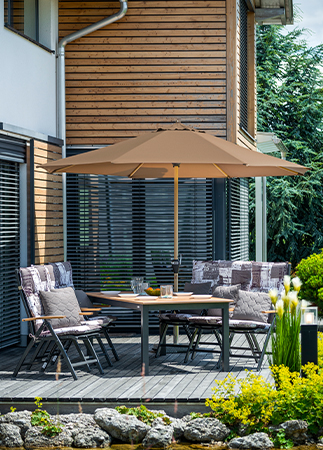Gartenterrasse mit Sitzgruppe, großem Sonnenschirm und Esstisch vor einem Wohnhaus mit Holzfassade