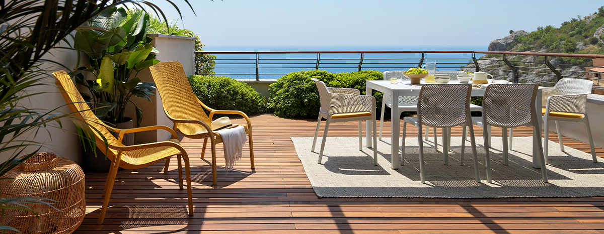Terrasse mit zwei Net Lounge Gartensesseln in Senape, Tisch Rio 210 in Weiß und vier Net Gartenstühlen in Tortora vor Meerblick
