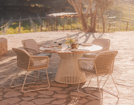 Niehoff Garden runder Gartentisch Acore mit vier Armlehnstühlen Lido auf Steinboden im Sonnenlicht