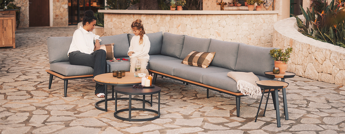 SERRA Loungegruppe mit grauem Ecksofa, Holzelementen und Couchtisch auf Naturstein-Terrasse, Frau und Kind sitzen zusammen
