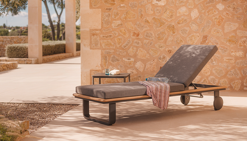 Niehoff Garden Vale Sonnenliege mit Polster in Anthrazit und Malta Loungetisch an einer hellen Steinmauer auf einer Terrasse